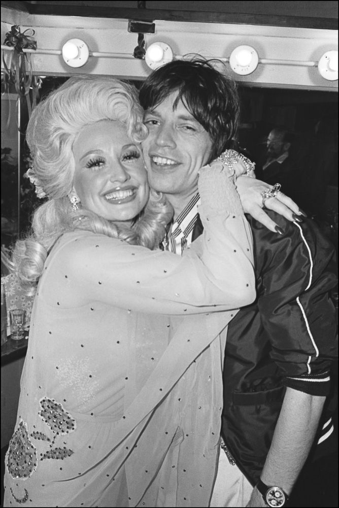Country music star Dolly Parton hugs rock star Mick Jagger backstage after her Bottom Line concert. 5/14/77 (Allan Tannebaum)
